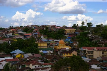 aerial view of a dense hillside village with a mosque dome under a cloudy blue sky