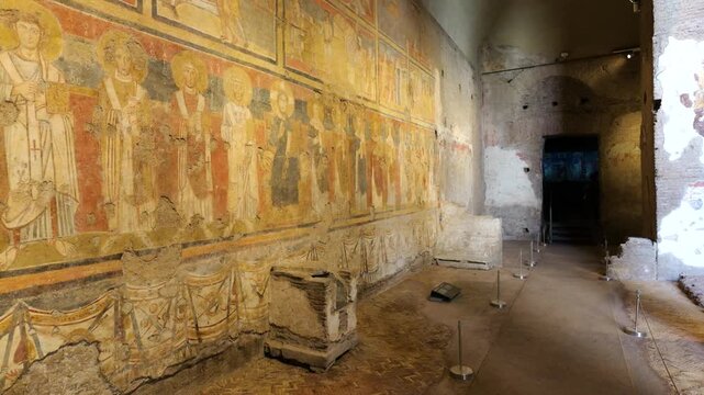 dim ancient hall fresco lined walls haloed religious figures vibrant colors bordered by drapery motifs stone fragments roped walkway rome italy fresco-lined roman interior art 
