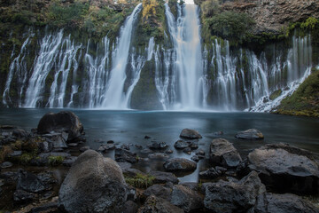 Fototapeta premium Burney Falls in early dawn light with stones in the foreground.