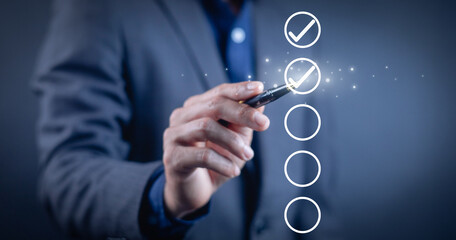 Businessman holding pen and selecting virtual checklist with check mark icons, representing...