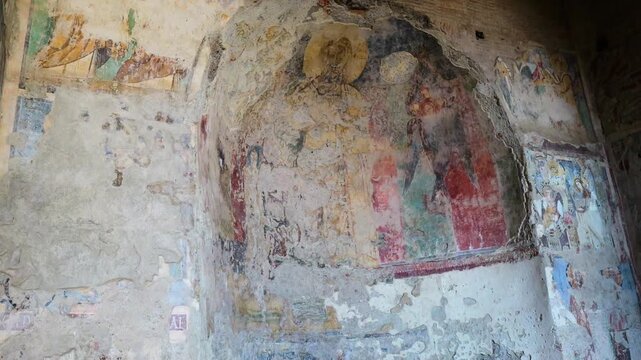 heavily weathered fresco depicts faint haloed figures muted colors missing plaster patches clearer religious fragments nearby curved wall rome italy roman artwork ancient painting 