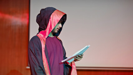 Indian young adult gen z male man standing wear outfit dress hold script paper do play scenes practice indoor hall stage. Teen age boy guy read story line talk speak day time college campus room place