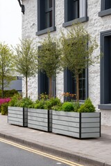 Colorful planters filled with vibrant flowers and lush trees adorn the area in front of a building featuring gray walls and expansive windows, all bathed in the bright light of daytime