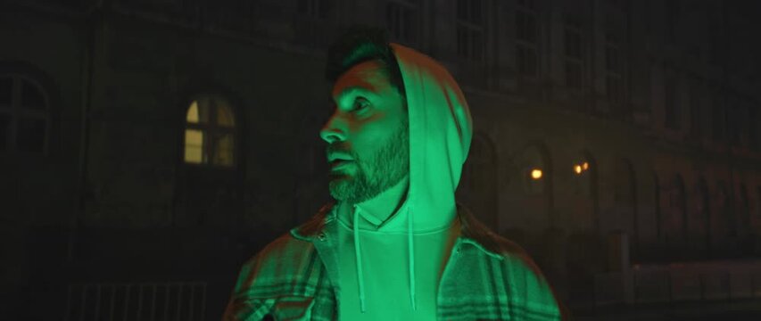 Urban individual in reflective clothing gazing thoughtfully beneath luminous neon street illumination at night