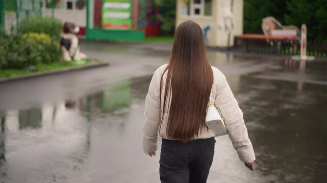 young woman walking on wet pavement, long braided hair, puffy jacket, canvas bag, puddles reflecting storefront signs, empty bench and cafe terrace, overcast sky, slow cinematic pacing, introspective