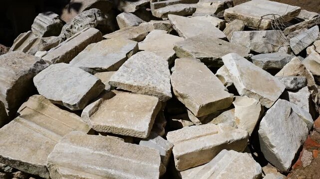 sunlit pile pale weathered marble limestone blocks broken architectural fragments chisel marks dusted surfaces centuries wear remain visible tempio del divo romolo rome italy roman empire emperor 