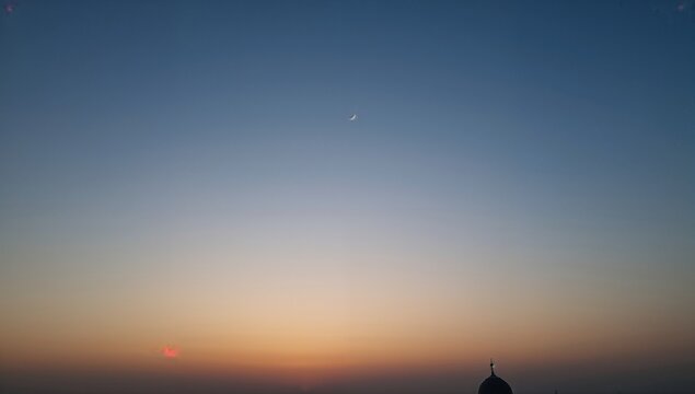 Faint crescent moon hangs high above a mosque dome silhouetted against a serene twilight gradient sky at dusk - Powered by Adobe