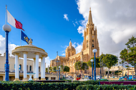 Ghajnsielem, Gozo, Malta &ndash; parish church with tall tower and classical pavilion on the village square, sunny sky and neat park