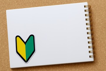 白いノートに貼られた初心者マークがこれから学び始める人の第一歩と入門段階を象徴するイメージ