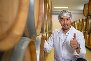 Expertise male Japanese wine maker working and inspecting wine fermenting from oak barrels in basement