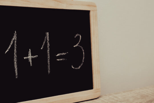 Incorrect math equation one plus one equals three written in chalk on a blackboard