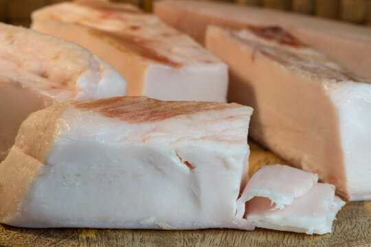 thick blocks of raw pork fatback resting on a wooden board, featuring thin shavings that reveal the smooth, white texture of the lard.