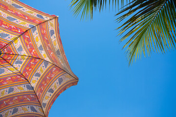 Colorful Beach Umbrella and Palm Leaves Against Blue Sky