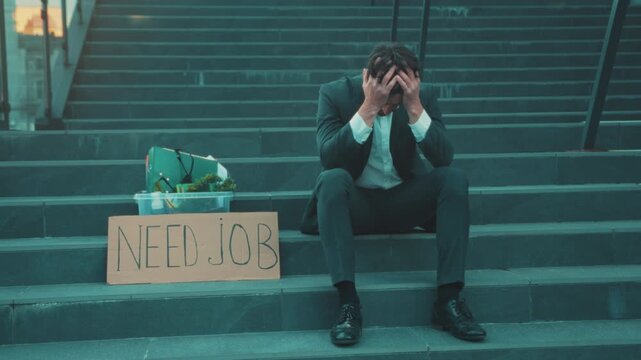 Individual seated anxiously near cardboard sign, Urban worker appears anxious amidst financial hardship signs