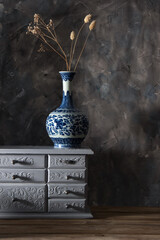 A ceramic vase on a light chest of drawers against a gray wall
