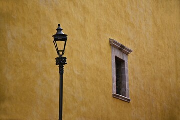 Antique stone window and a cast iron lantern on the exterior ochre stucco wall of the Catedral Basílica Colegiata de Nuestra Señora de Guanajuato in the World Heritage Site of Guanajuato in Mexico.