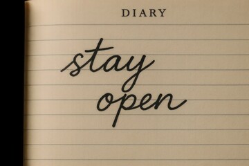 A close-up of an open diary with the words 'stay open' written in elegant cursive on a lined page. The background is dark, emphasizing the text.