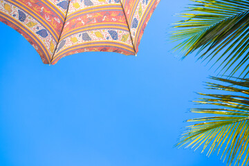 Colorful Beach Umbrella and Palm Leaves Against Blue Sky