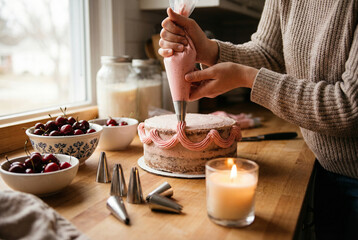 hands piping pink buttercream swags on a small cake