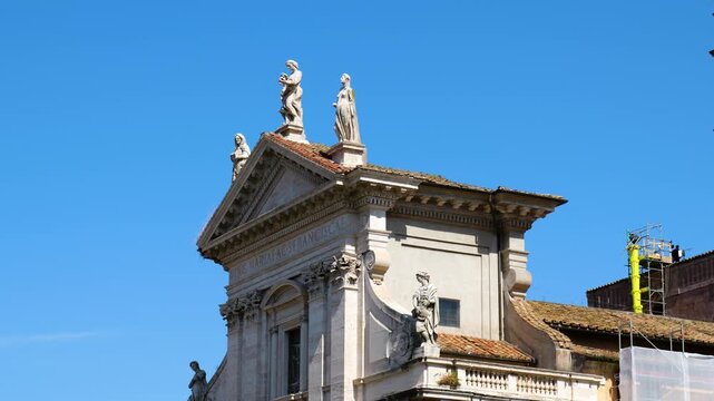 roman baroque church facade sculpted stone statues along pediment roofline pale masonry contrasts vast cloudless blue sky rome upward view italy empire emperor 
