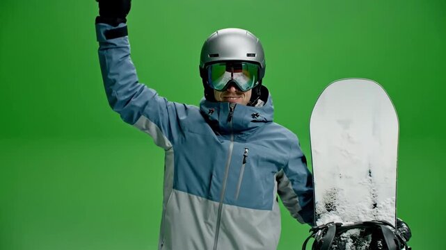 A triumphant snowboarder, wearing cool blue gear, celebrates his competition victory while holding a snowy board in a studio green screen shot.