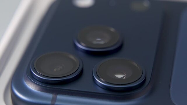 A rotating smartphone camera module reveals three lenses with metallic rings and glass surfaces. Macro focus emphasizes precision engineering and modern mobile photography.