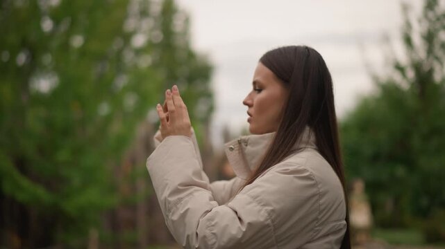 caucasian woman side profile photographing with smartphone, beige puffer jacket and long braided hair, wooden fence and backyard bokeh, overcast soft light, focused expression, framing vertical shot