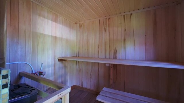 cozy sauna room with light wooden walls and ceiling, built-in wooden bench, upper shelf, tiled stove corner, small window for ventilation