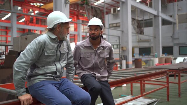 Senior factory worker mentoring younger colleague on production floor