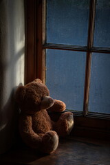Teddy bear on the windowsill with glass covered in droplets