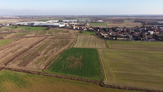 Panoramic Farmland View. An expansive aerial view showcases a patchwork of vibrant fields, interspersed with residential structures and commercial facilities. Italy, Lombardy