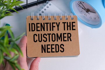 Notepad with IDENTIFY THE CUSTOMER NEEDS text on keyboard with felt-tip pens and calculator on wooden background