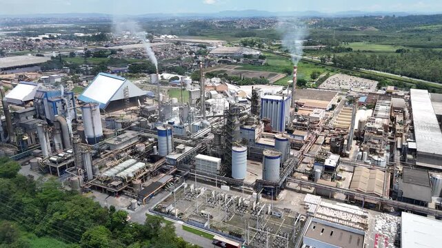 Vis&atilde;o drone 4k a&eacute;rea da ind&uacute;stria de papel e celulose destaca a magnitude da planta industrial, chamin&eacute;s e caldeiras operando em um sistema produtivo cont&iacute;nuo.