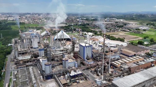 Vista a&eacute;rea de ind&uacute;stria de papel e celulose com infraestrutura robusta, caldeiras e chamin&eacute;s liberando vapores do processo industrial cont&iacute;nuo.