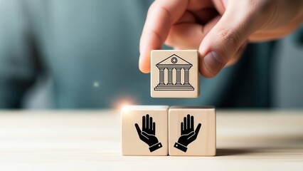 Hand holding a wooden block with a bank building icon, placed above two blocks with hand icons, symbolizing financial services, government support, or legal institutions interacting with people.
