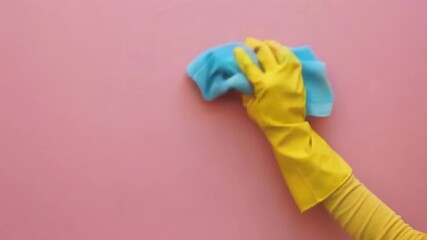 A yellow glove with a blue cloth carefully wipes the pink surface, illustrating cleaning and cleanliness, which is ideal for the background of an advertisement for household chemicals or home care tip