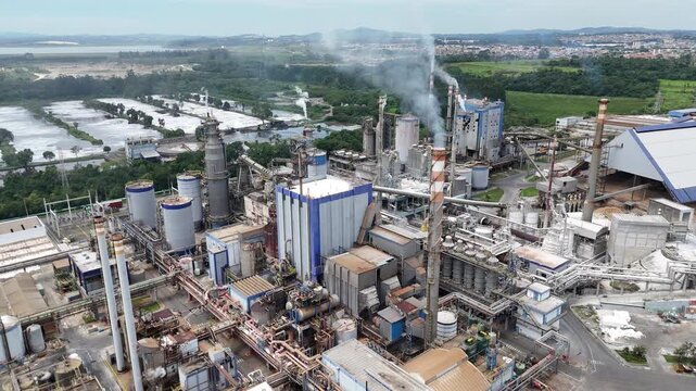 Vis&atilde;o a&eacute;rea v&iacute;deo 4k de f&aacute;brica de papel e celulose destaca caldeiras e chamin&eacute;s com vapores, evidenciando gera&ccedil;&atilde;o de energia t&eacute;rmica e produ&ccedil;&atilde;o industrial em larga escala.