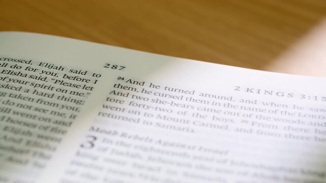 Macro footage of English Bible with pages turning to reveal 2 Kings book chapter 3. Crisp printed text, smooth motion, and soft lighting ideal for faith, study, worship, and educational media