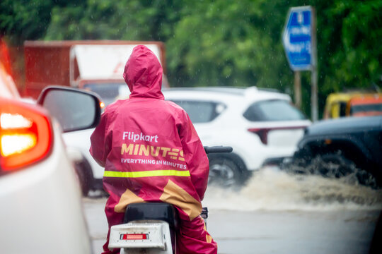 Rider of hyperlocal quick commerce delivery app Flipkart minutes wearing a raincoat and riding through the streets showing the increase of 10 min fulfilment in major cities