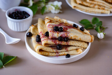 Thin pancakes on a white plate for breakfast. Delicious pancakes with berry jam. Close-up