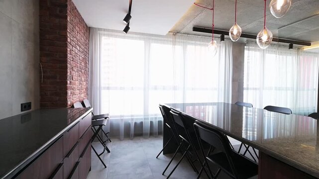 sleek loft-style kitchen with dark countertops, exposed brick wall, modern pendant lights, large windows with sheer curtains, and a minimalist dining setup 