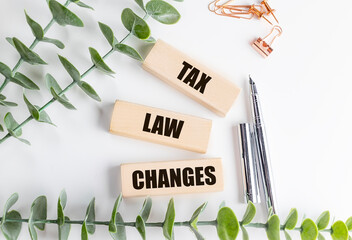 Wooden blocks with text tax law changes on white desk with green plant, pens and stationery items