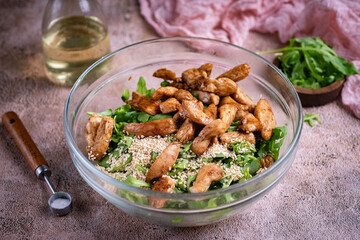Salad with chicken, arugula, and sesame seeds on a brown background. A delicious salad for breakfast. Close-up