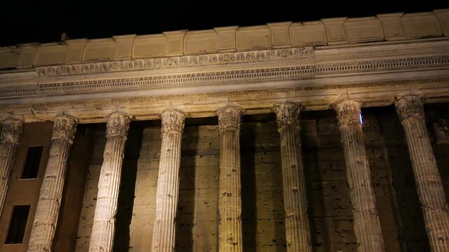 night time ancient roman temple facade fluted corinthian columns carved entablature golden light weathered stone glows piazza di pietra / hadrian up close rome italy empire 