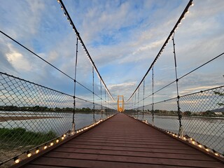 A picturesque view of a suspension bridge stretching over water, framed by scenic clouds and a...