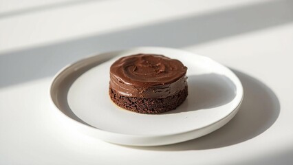 A simple mini chocolate cake on a white plate, minimalist style, soft natural lighting, smooth chocolate frosting, clean background, realistic food photography