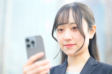 オフィス街でスマホを使用するスーツのビジネスウーマン