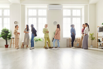 Women meet at networking conference and discuss business ideas. Young diverse multi racial ladies talking while standing in spacious light office interior with large windows. Communication concept