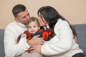 Parents kissing their toddler while sitting together on a couch indoors.