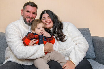 Happy parents holding their toddler while sitting together on a couch in a cozy indoor setting.